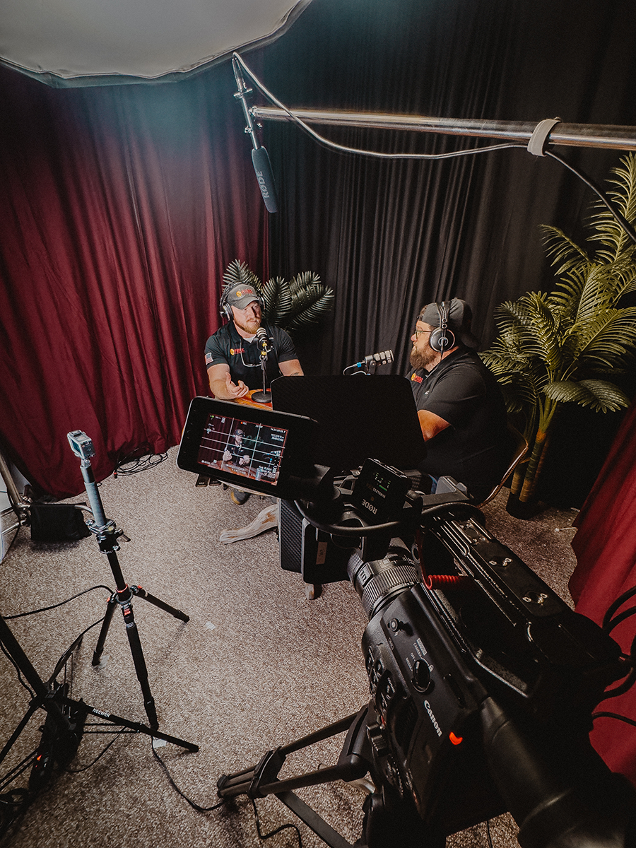 Behind the scenes of an Into the Lion’s Den recording, with cameras, lights and two people at microphones
